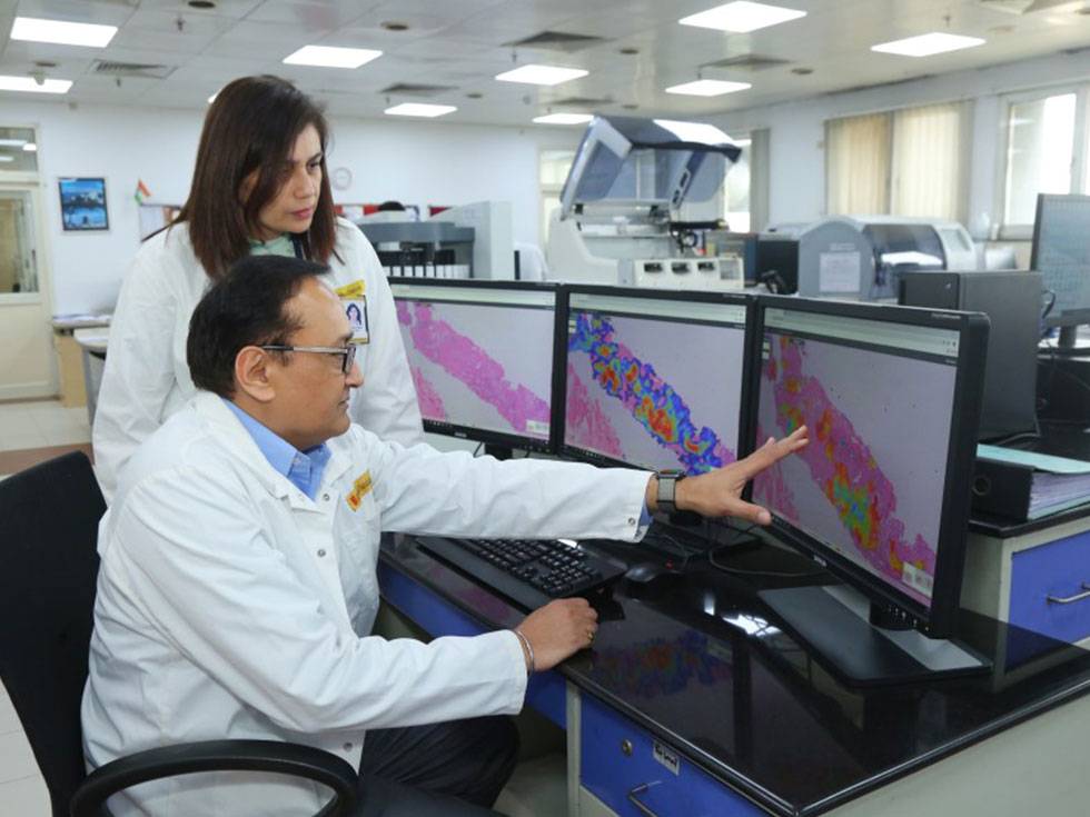 A pathologist discussing with a colleague a digital scan on the monitor screen.
